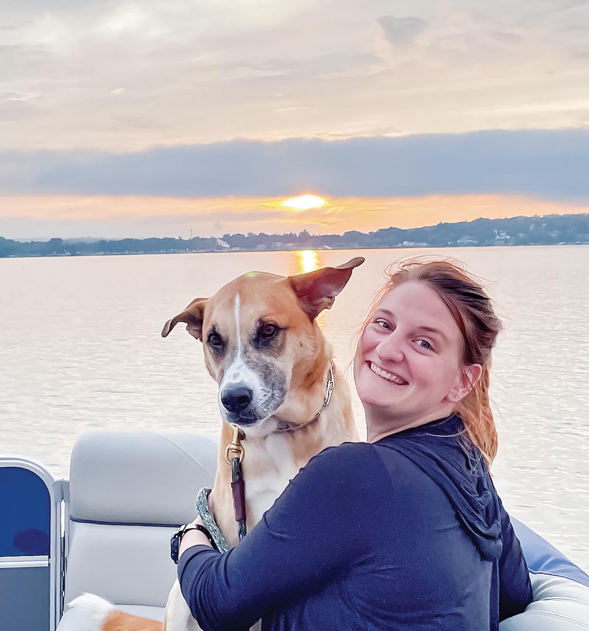 Pokoj Family - girl smiling with her dog on the boat while the sun sets