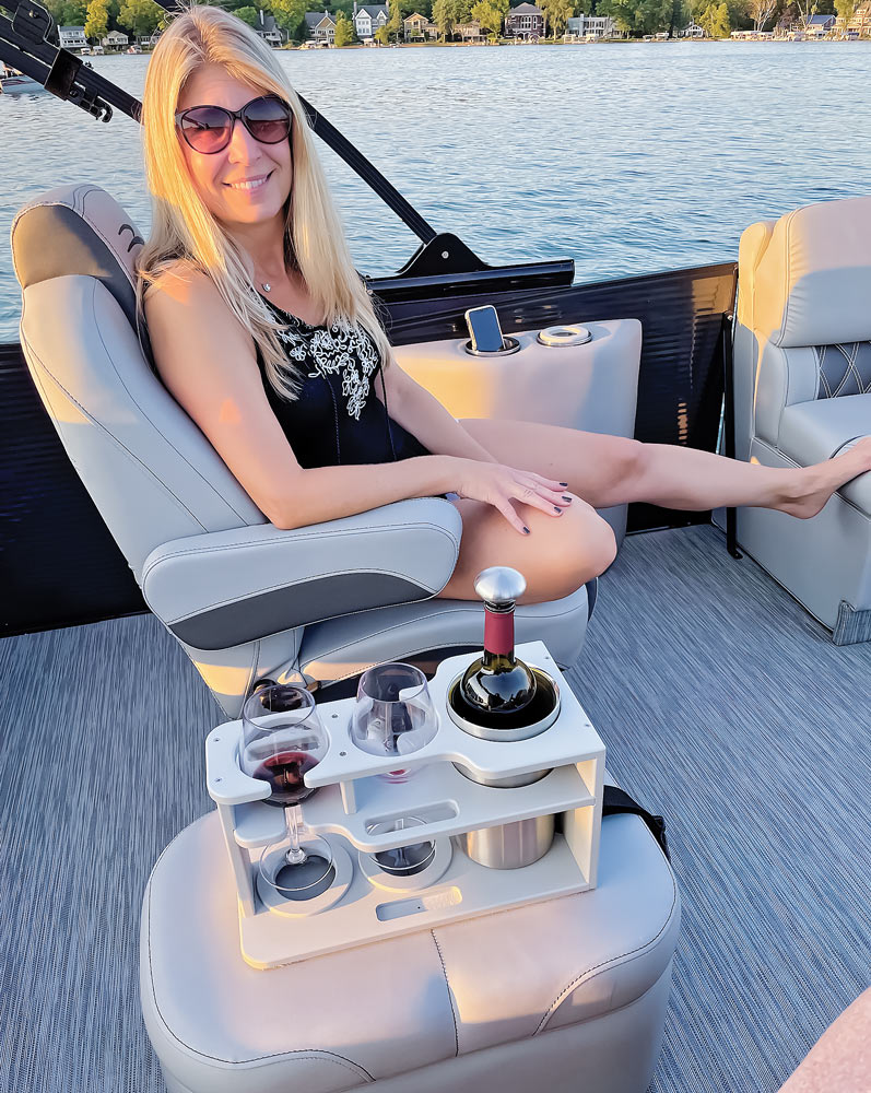 a woman sits on a boat smiling, using the convertible drink caddy to hold wine glasses and a bottle