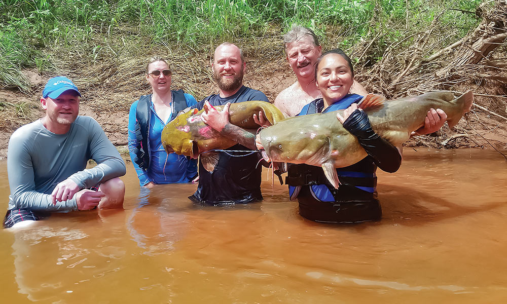 a group of five fishers smile with two hold large catfish