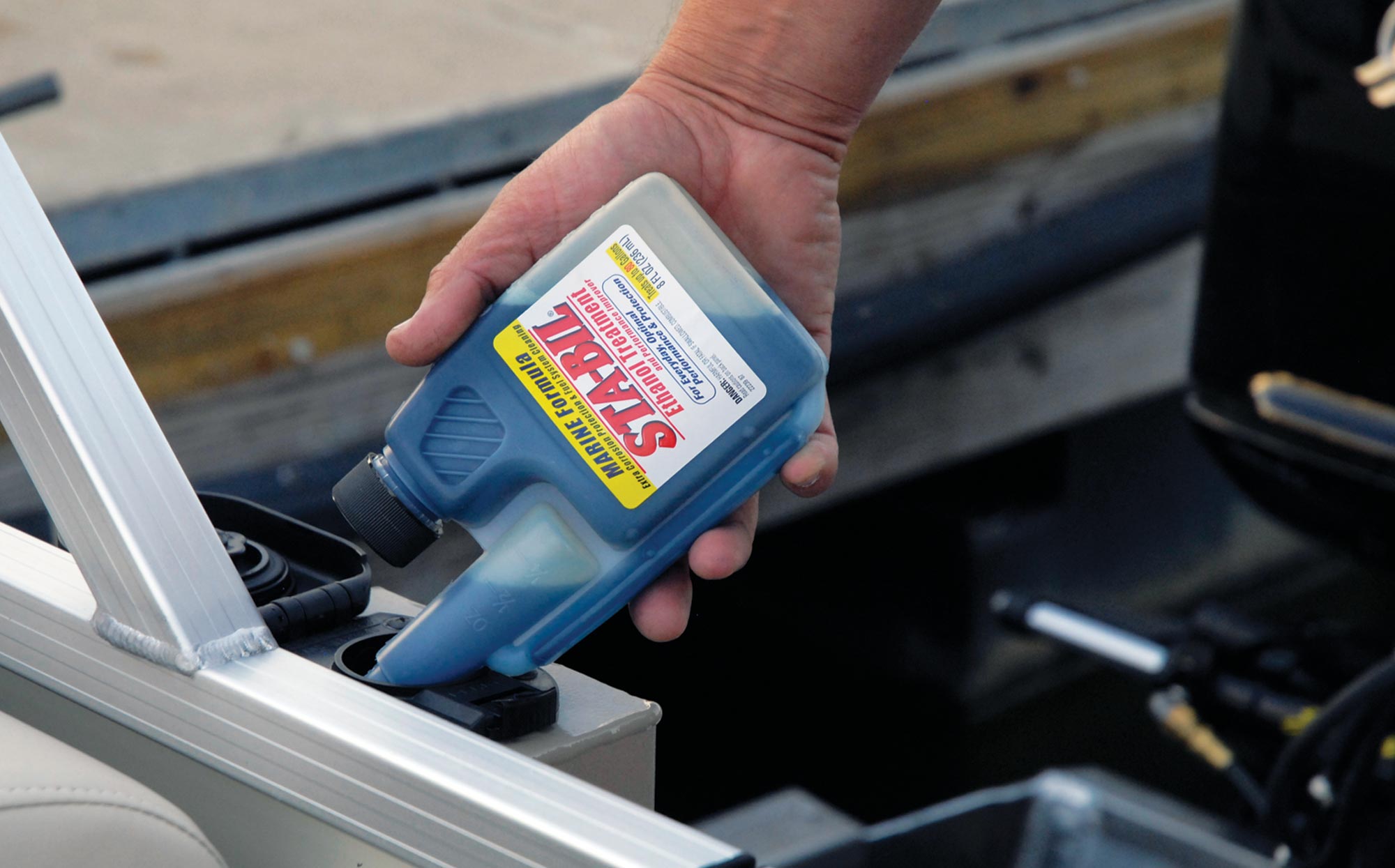 a hand pours Sta-Bil marine formula into a tank opening