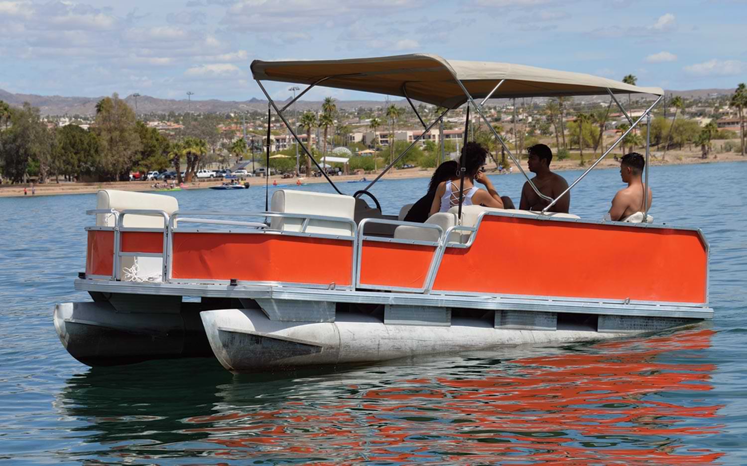 a group of people sit under a sunscreen on an orange pontoon on water