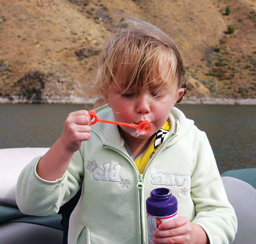 a little girl sits on a pontoon blowing bubbles