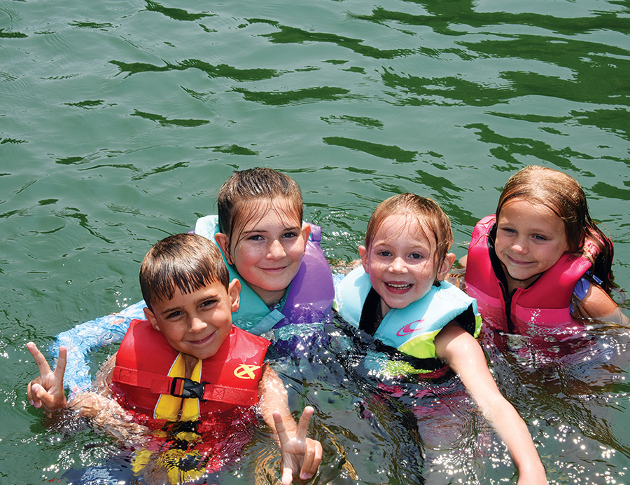 4 kids in lifejackets in the water smiling