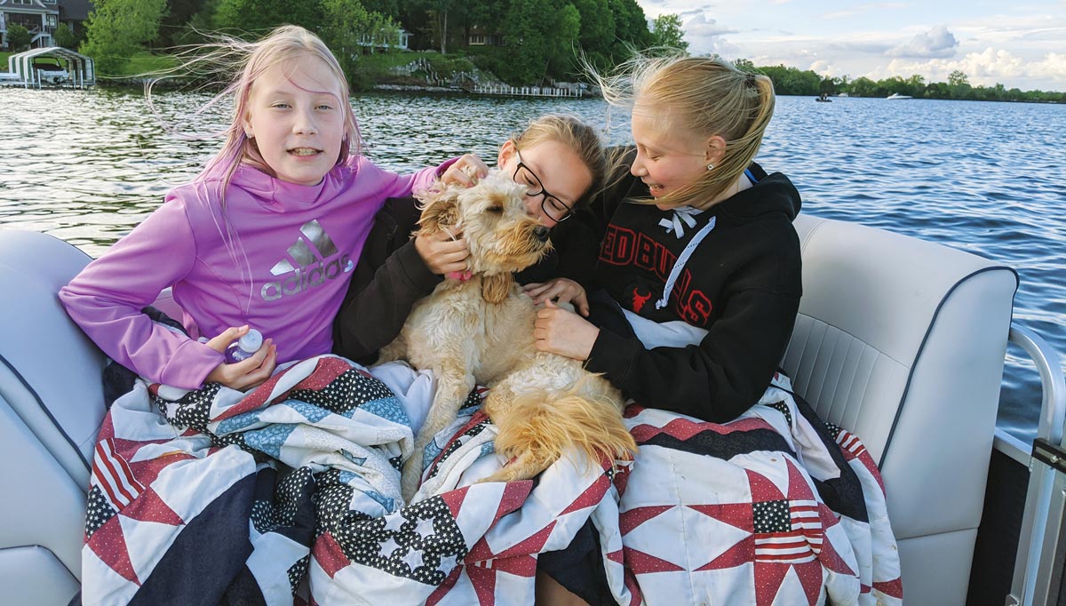 three girls and a dog sitting on a boat together