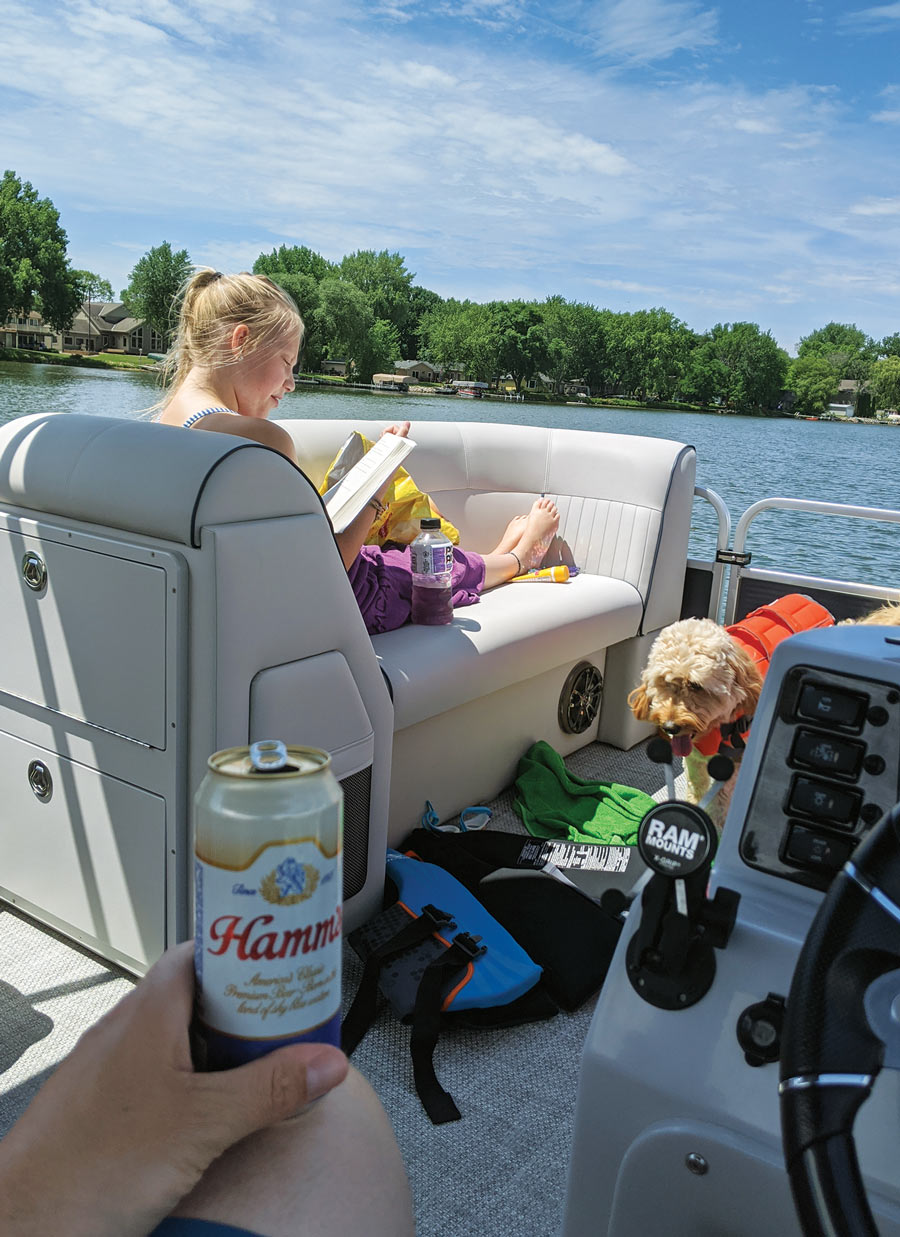 hand holding a beer and girl reading a book on boat