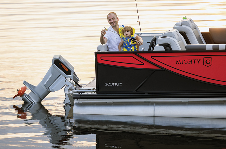 A young boy and his father fishing off the back of a red and black pontoon boat at sunset