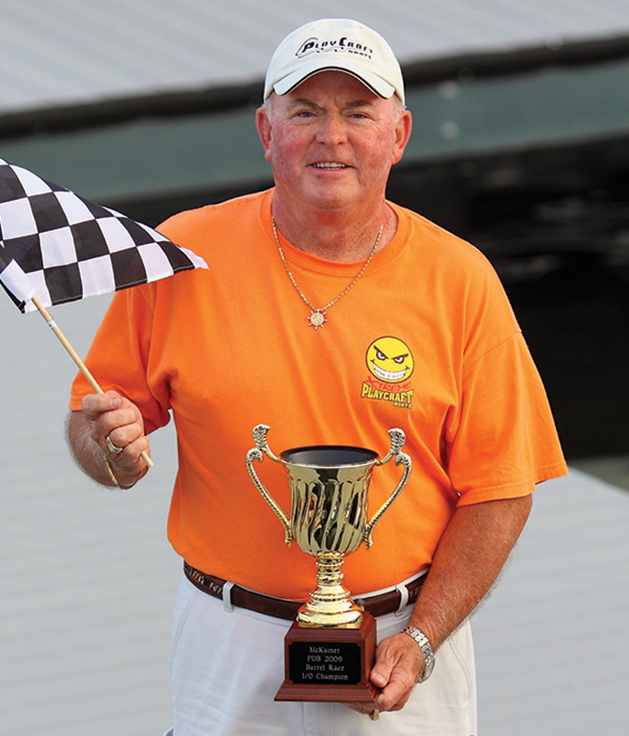 Jim Dorris in a bright orange shirt holding a trophy and racing flag on a boat dock