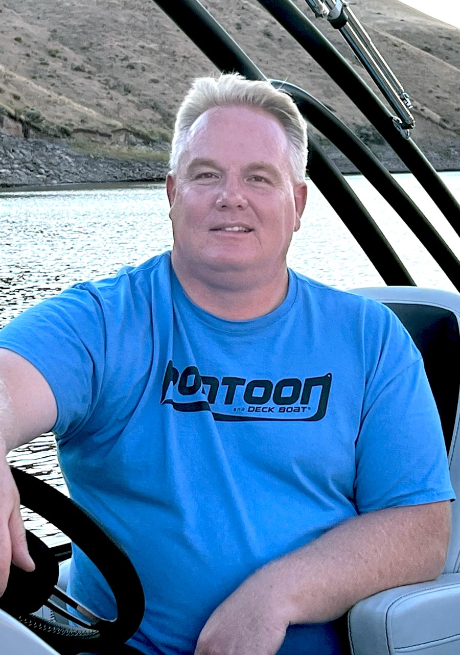 Brady Kay sitting in the drivers seat of a boat in a blue Pontoon and Deck Boat t-shirt