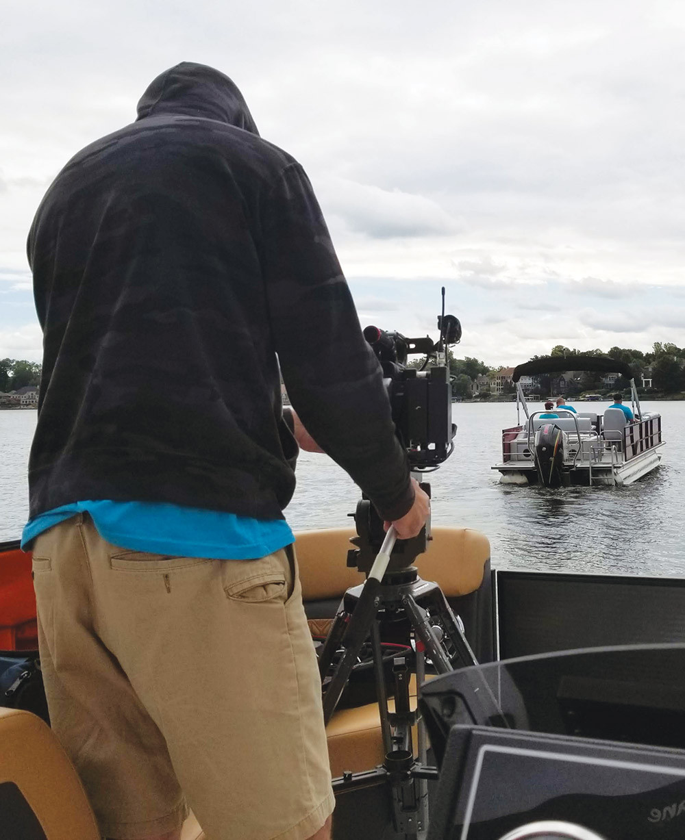 man with hood on using a camera on a tripod while on a boat