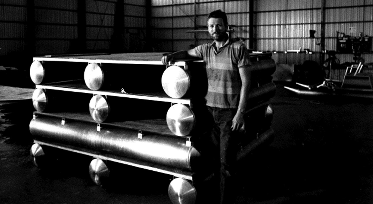 a black and white photo of a man standing near a stack of platforms and tubes