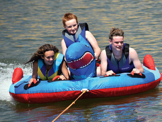 Three kids riding on a HO Sport Shark towable