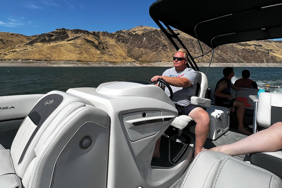 man driving boat with mountain scape behind him