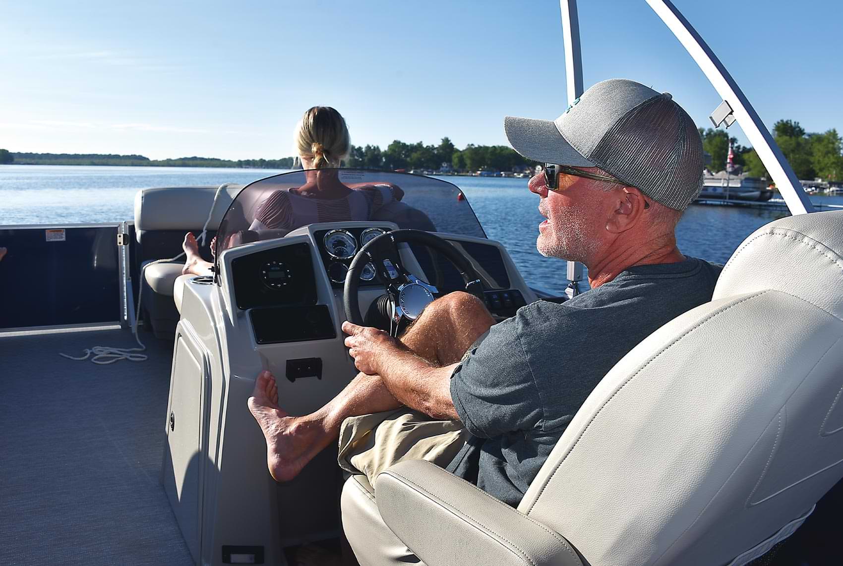 a man sits at the helm of a Sylvan pontoon out on the water