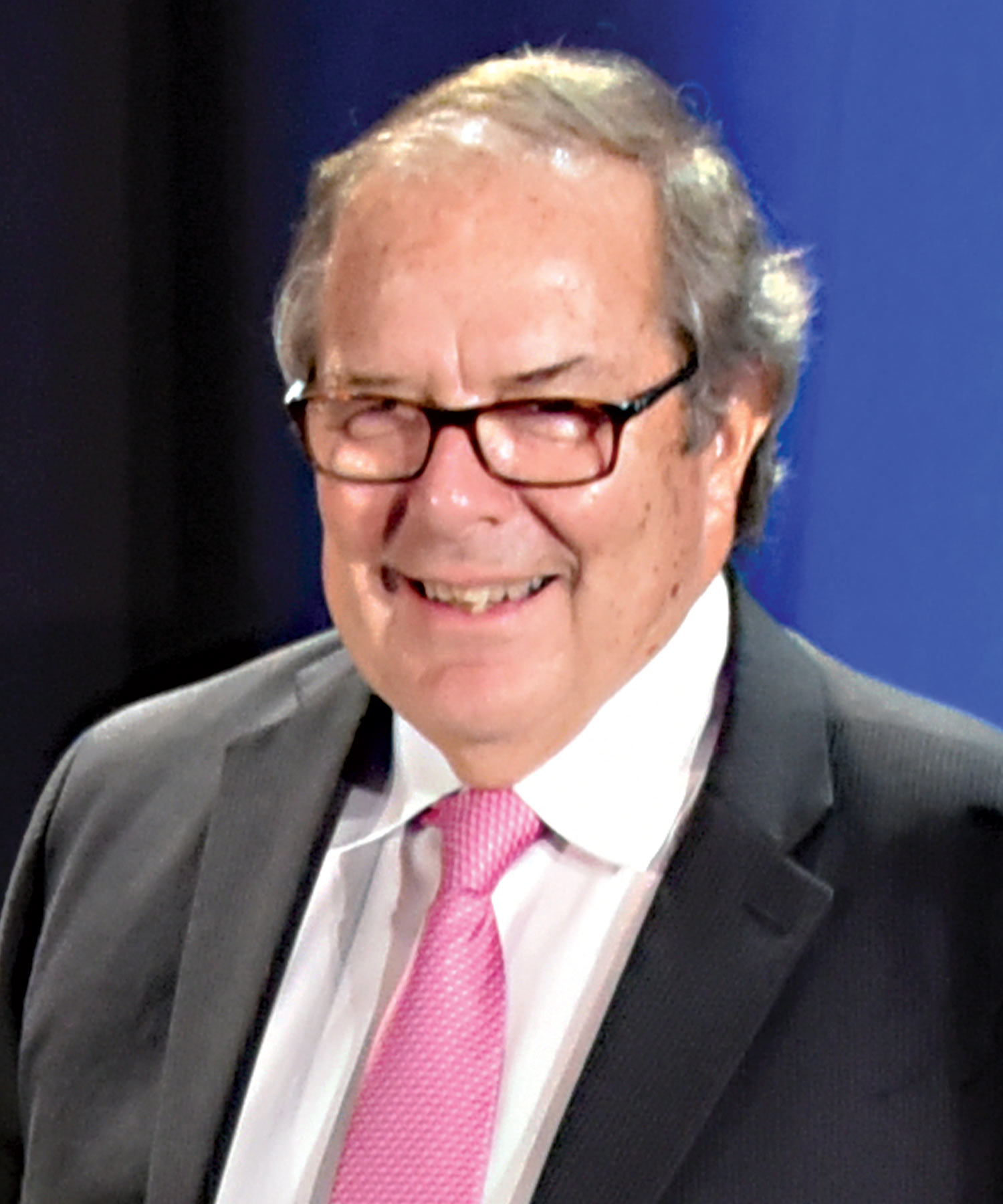 portrait of Doug Smoker wearing a suit, a pink tie and thick rimmed glasses