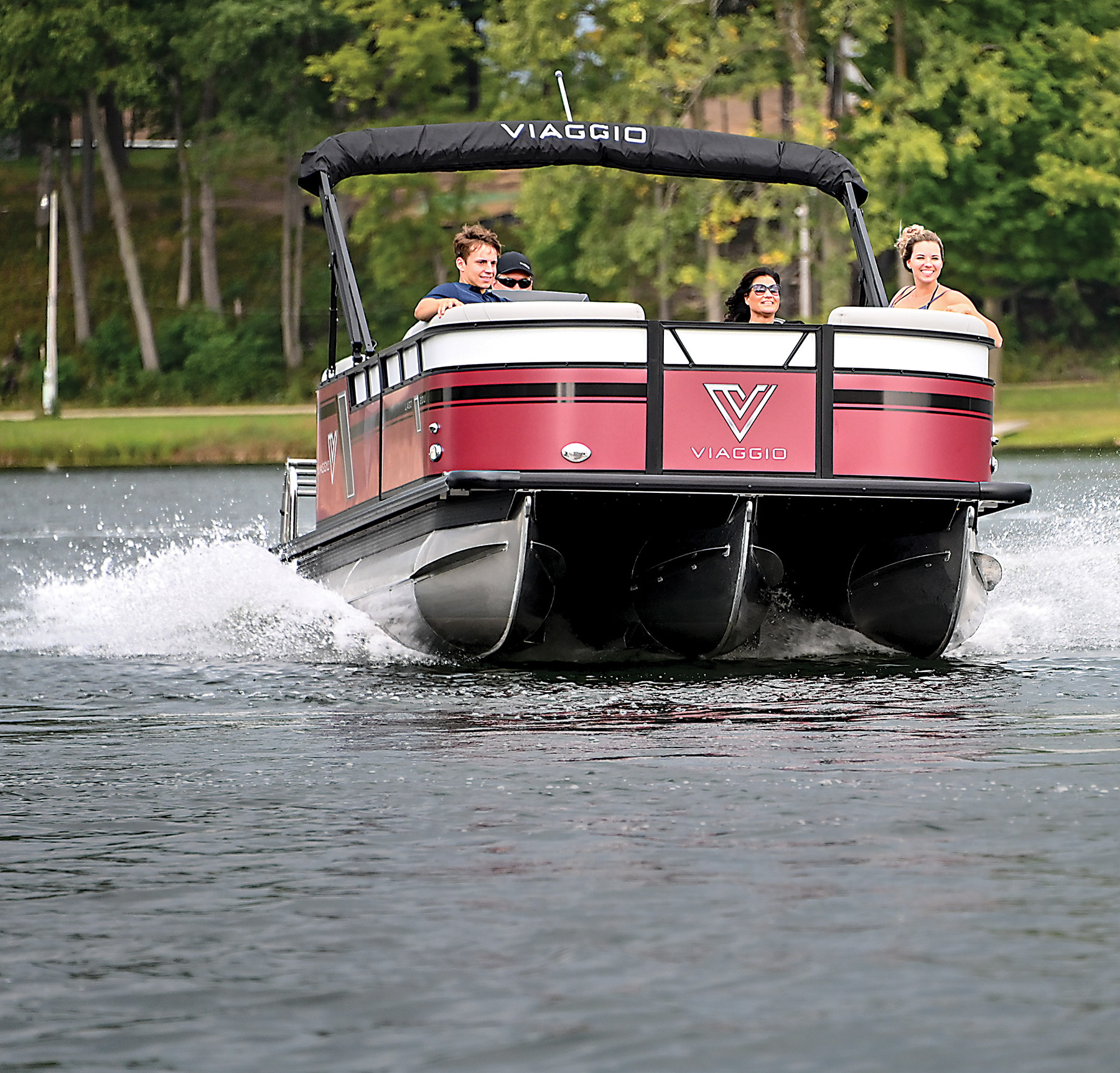 A landscape front photograph view of the Viaggio Lago 20U boat in red, black and grey cruising in the water outdoors with two guys and two girls inside smiling and enjoying a good time