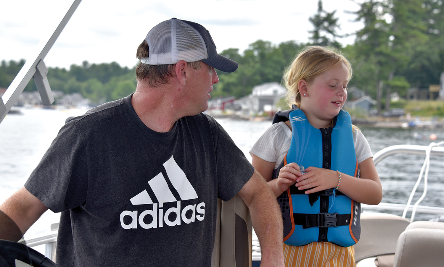 Charlie McGee sits at the helm of a pontoon looking back at his young daughter wearing a life vest