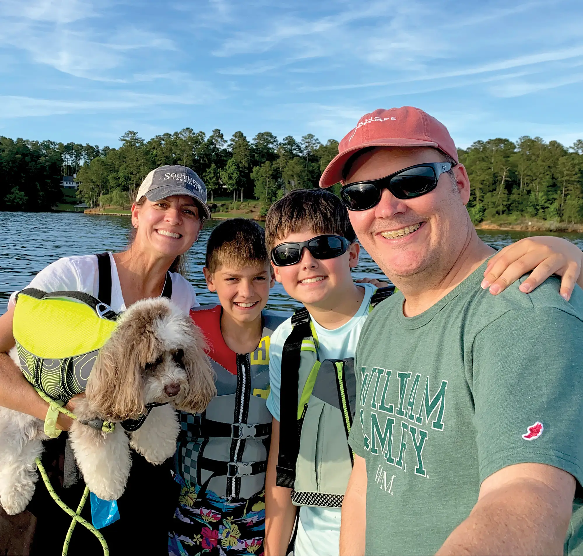 man takes a selfie with his wife, 2 sons, and dog on their pontoon