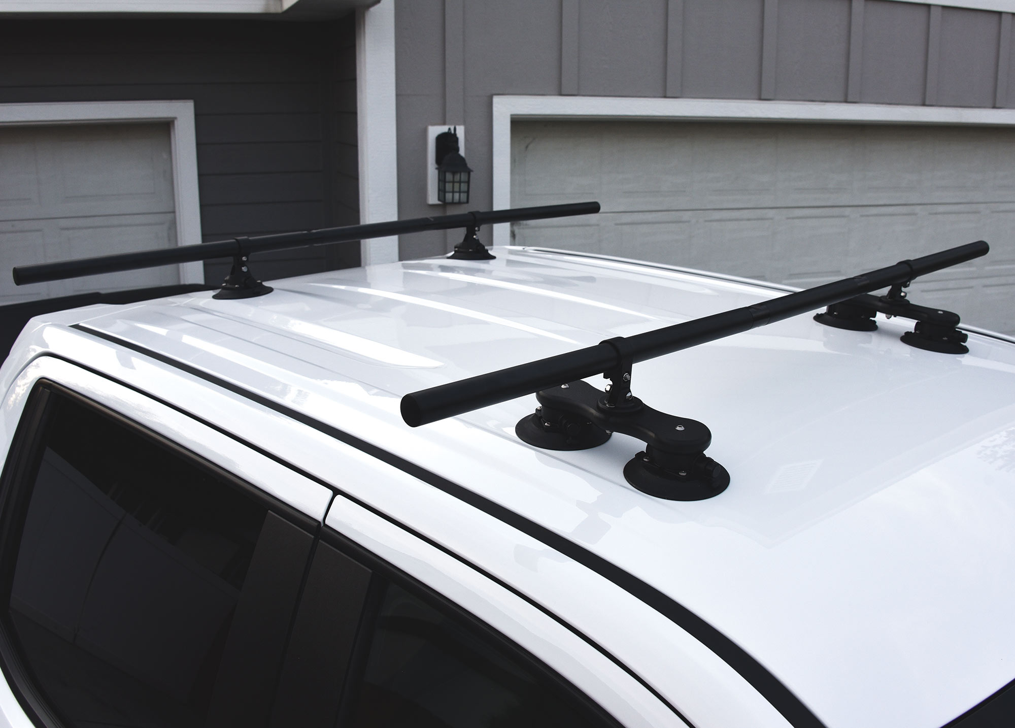 Close-up top angle photograph of SeaSucker Monkey Bars crossbar roof rack system installed on top of a white truck parked outside on a house driveway/in front of the garage