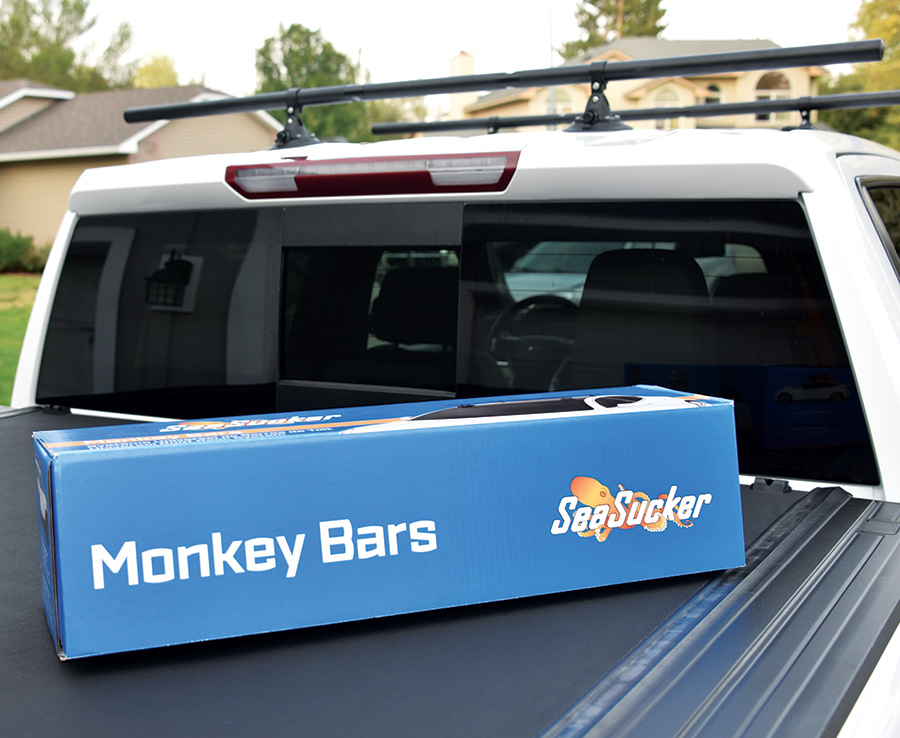 Close-up top rear photograph of SeaSucker Monkey Bars crossbar roof rack system product box on top of a white truck bed
