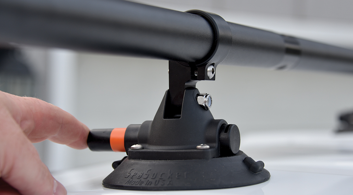 Close-up top angle photograph of a man's finger touching the black push/pump cap from the circular mount of the SeaSucker Monkey Bar crossbar roof rack system installed on top of a white truck