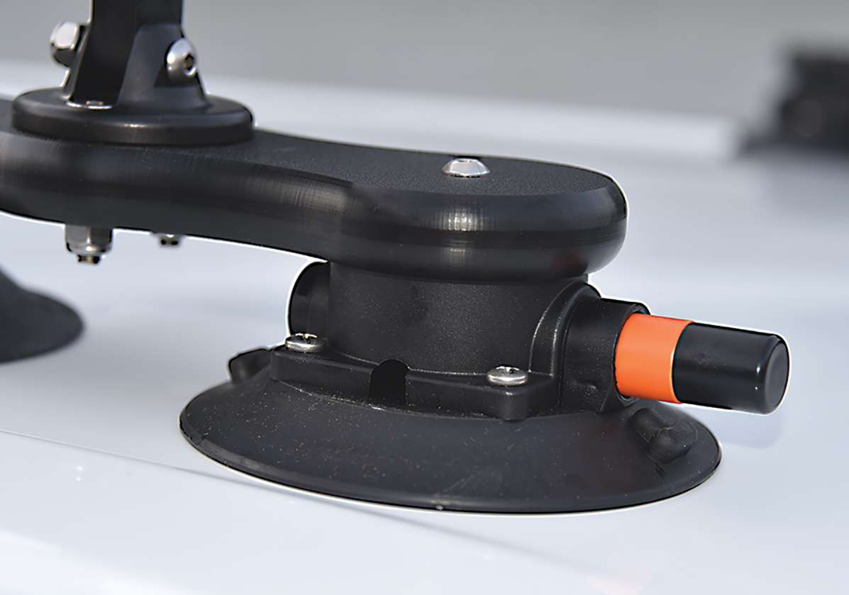 Close-up top angle photograph of a black push/pump cap inserted halfway into the circular mount with a little orange cushion pump cap remaining of the SeaSucker Monkey Bar crossbar roof rack system installed on top of a white truck
