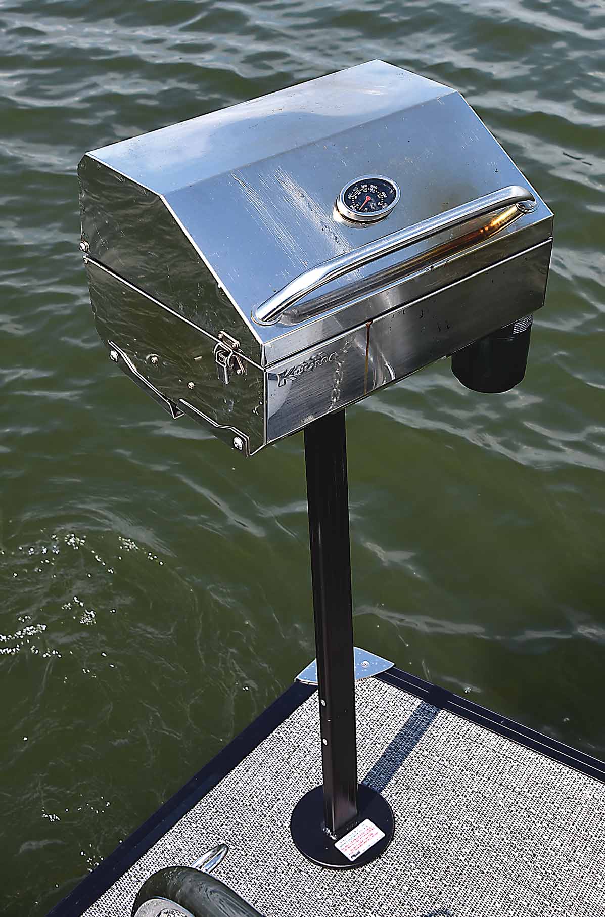 Close-up portrait photograph perspective of a closed small metal chrome colored mounted barbecue grill stand attached to the rear stern surface area of the pontoon boat motor vehicle (Lillipad Marine Flagpole/Grill Post)