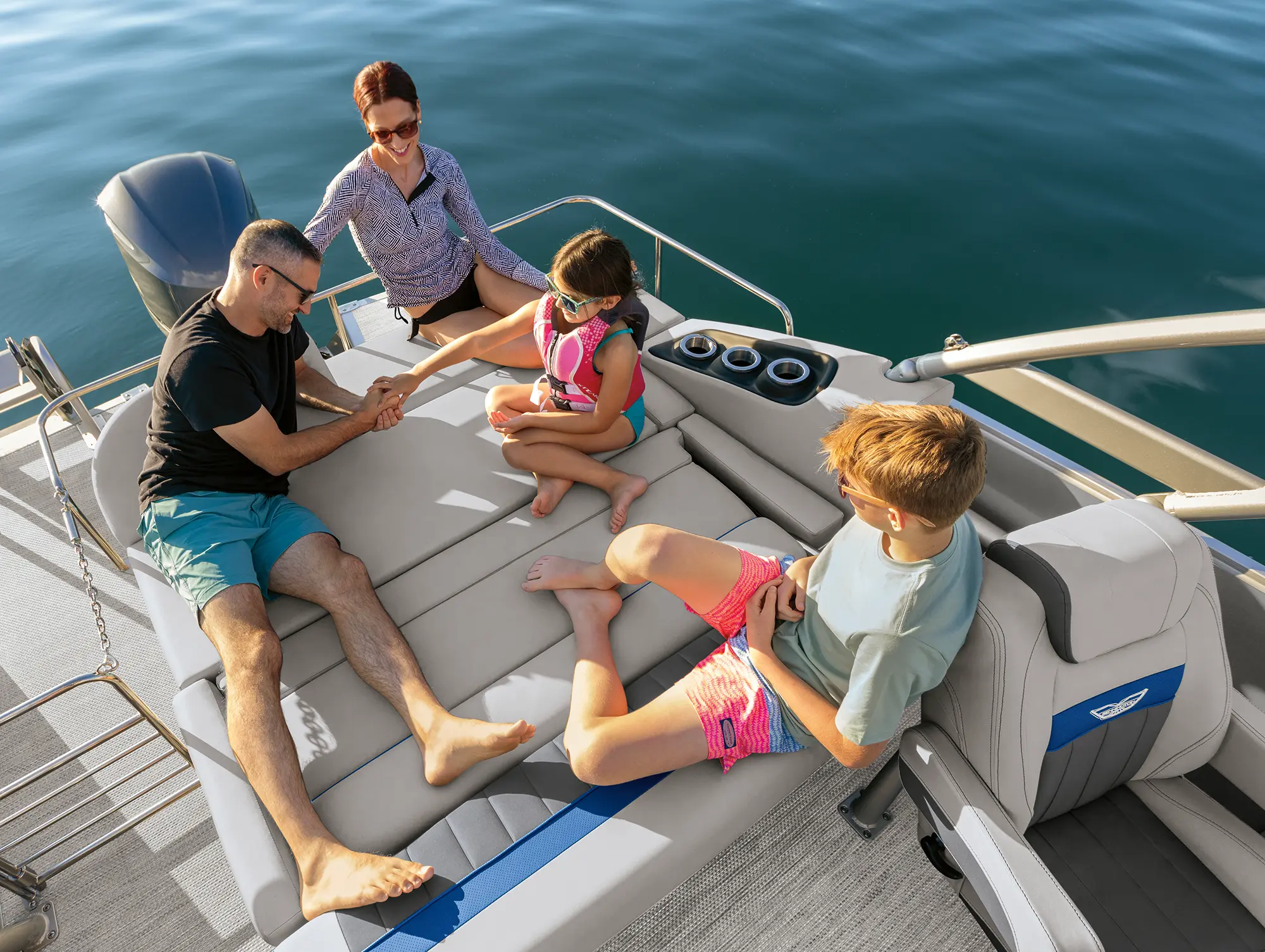 Family of four seen resting inside the Bennington Sport 24 LXSSBA pontoon motorboat vehicle out in the water during the day as all of them are wearing sunglasses and are in beach attire
