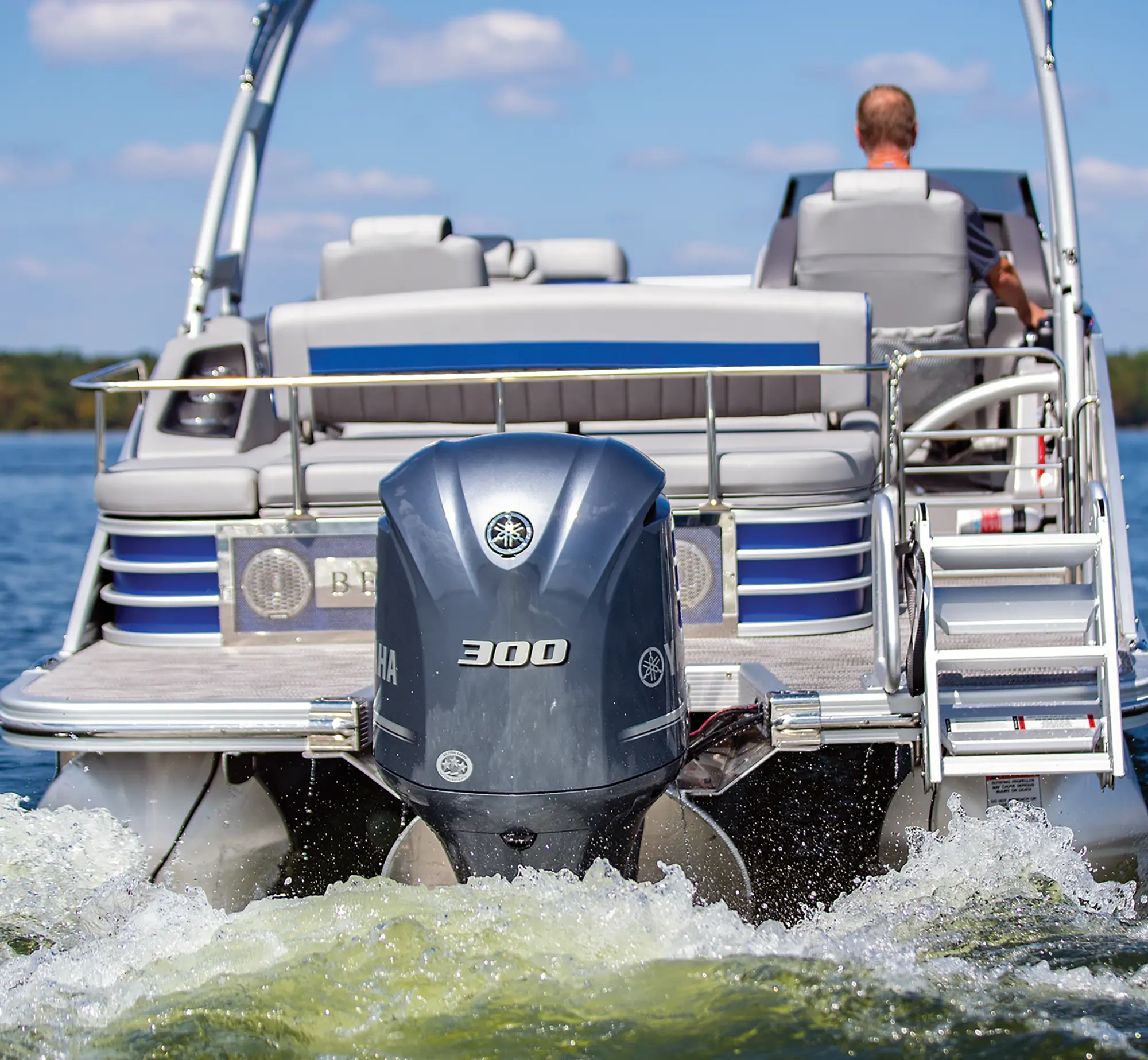 Close-up aerial rear view of the the Yamaha 300 Four Stroke outboard motor engine from the Bennington Sport 24 LXSSBA pontoon motorboat vehicle as a man is seen driving away out in the water during the day