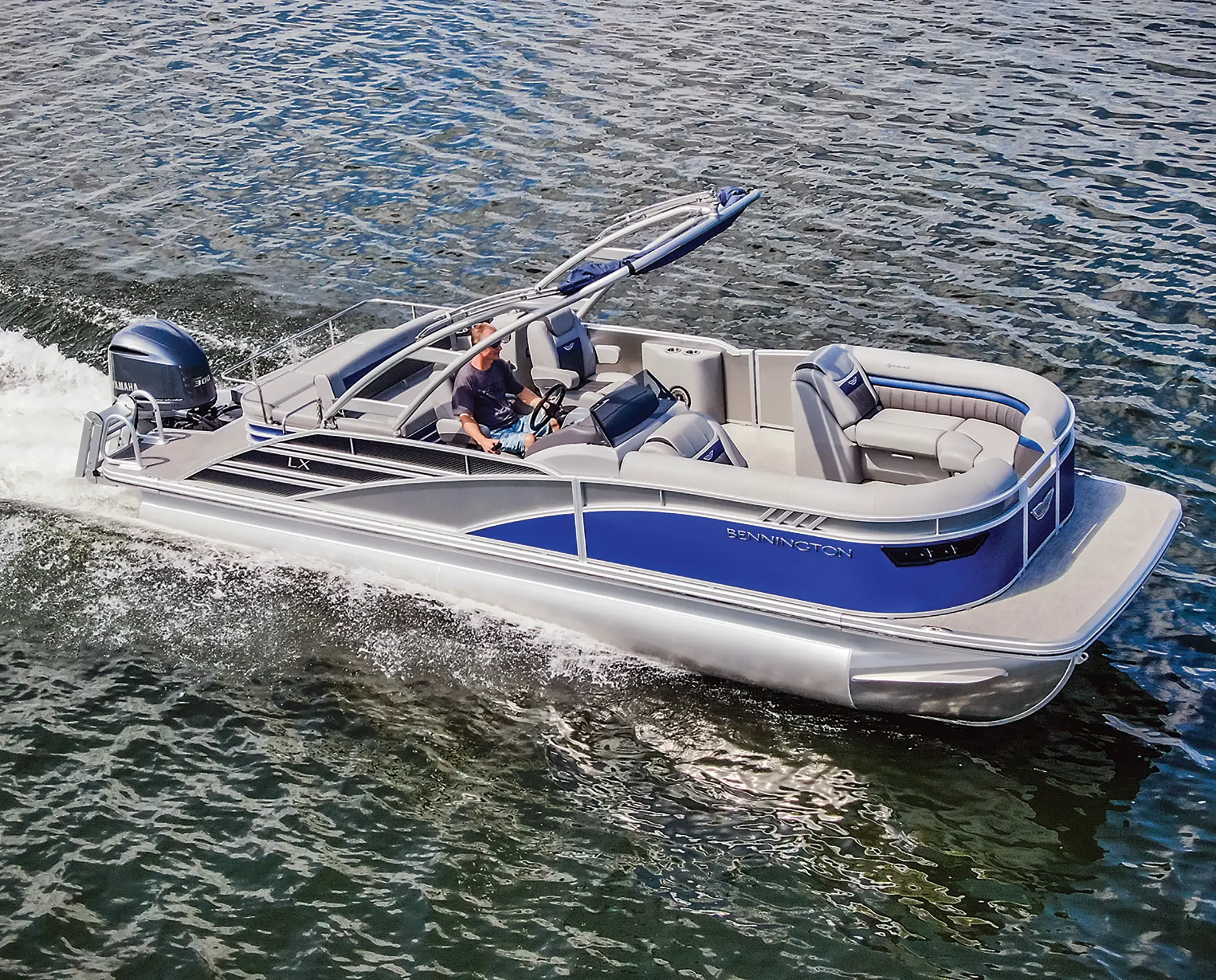 Aerial side view of the Bennington Sport 24 LXSSBA pontoon motorboat vehicle as a man is seen driving out in the water during the day