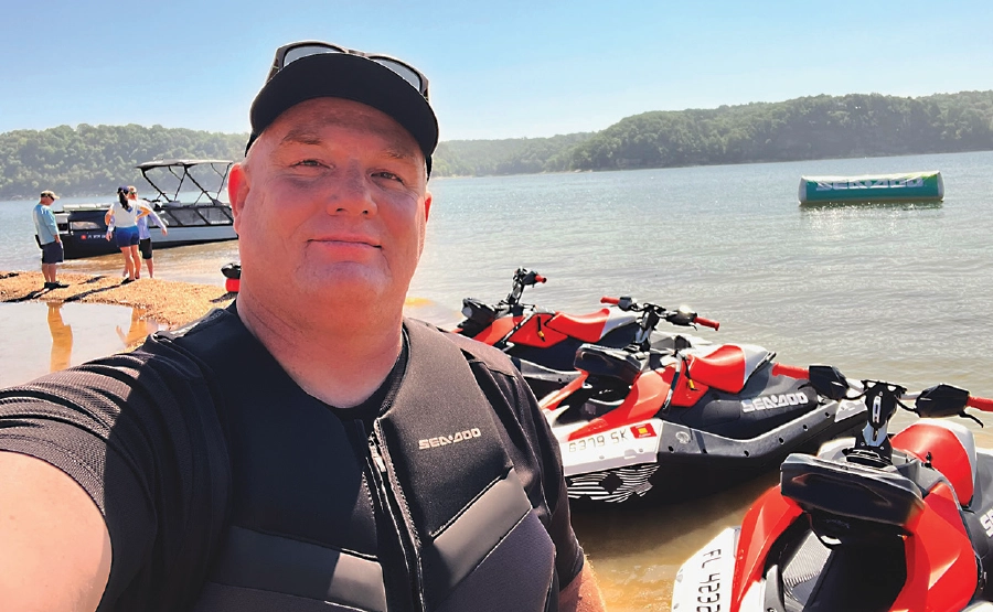 man taking selfie with lake and sea-doos behind him
