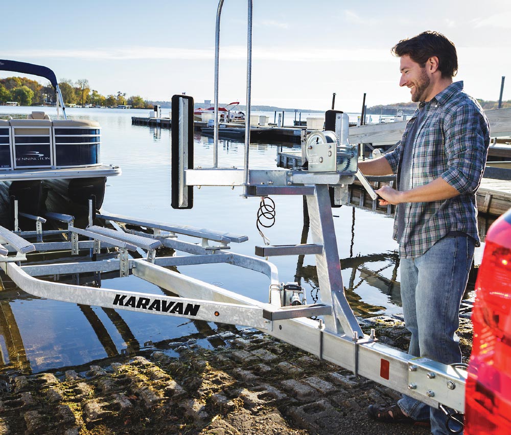 man in jeans and plaid button up smiling next to Karavan trailer in water