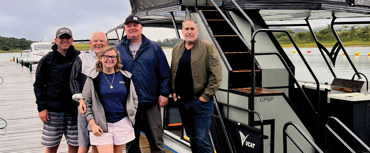 Jason Harris, VCAT owners Benedito Prado Neto and Valéria De Fusco Pereira, PDB Editor Brady Kay and Guillermo Troelsen stand together for a photo on a long pier beside a two level VCAT pontoon