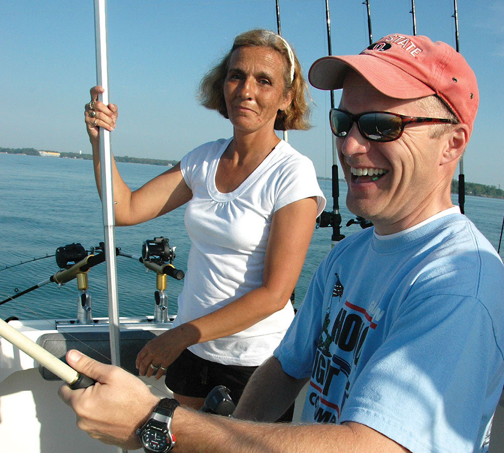 man and woman smiling while fishing on boat