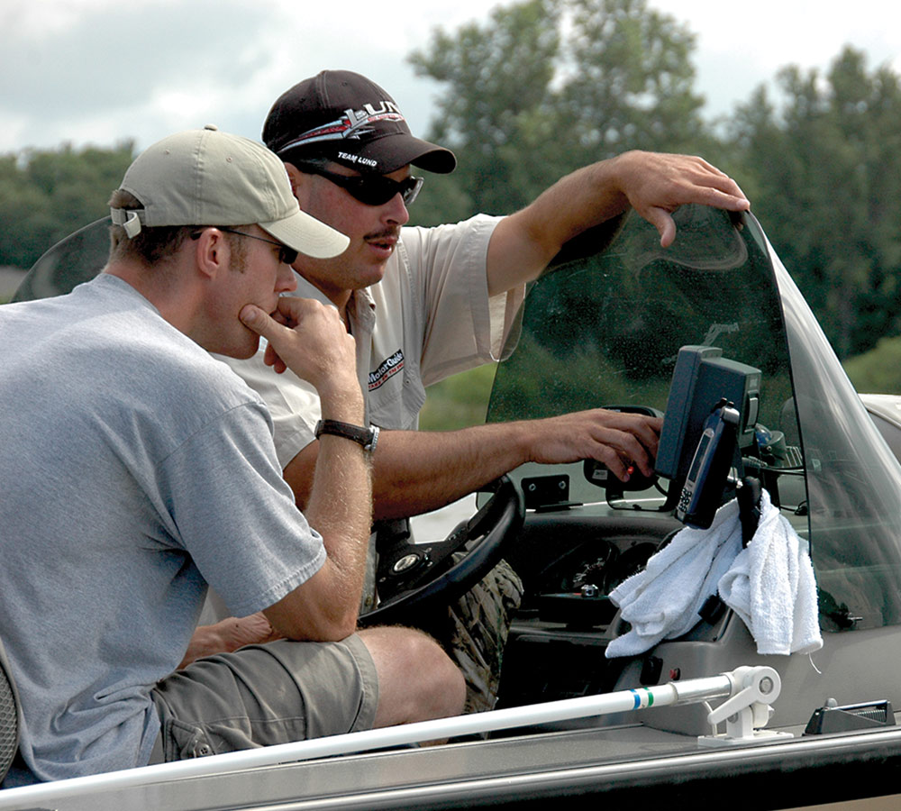two men looking at different devices stationed near the driver's seat of a boat