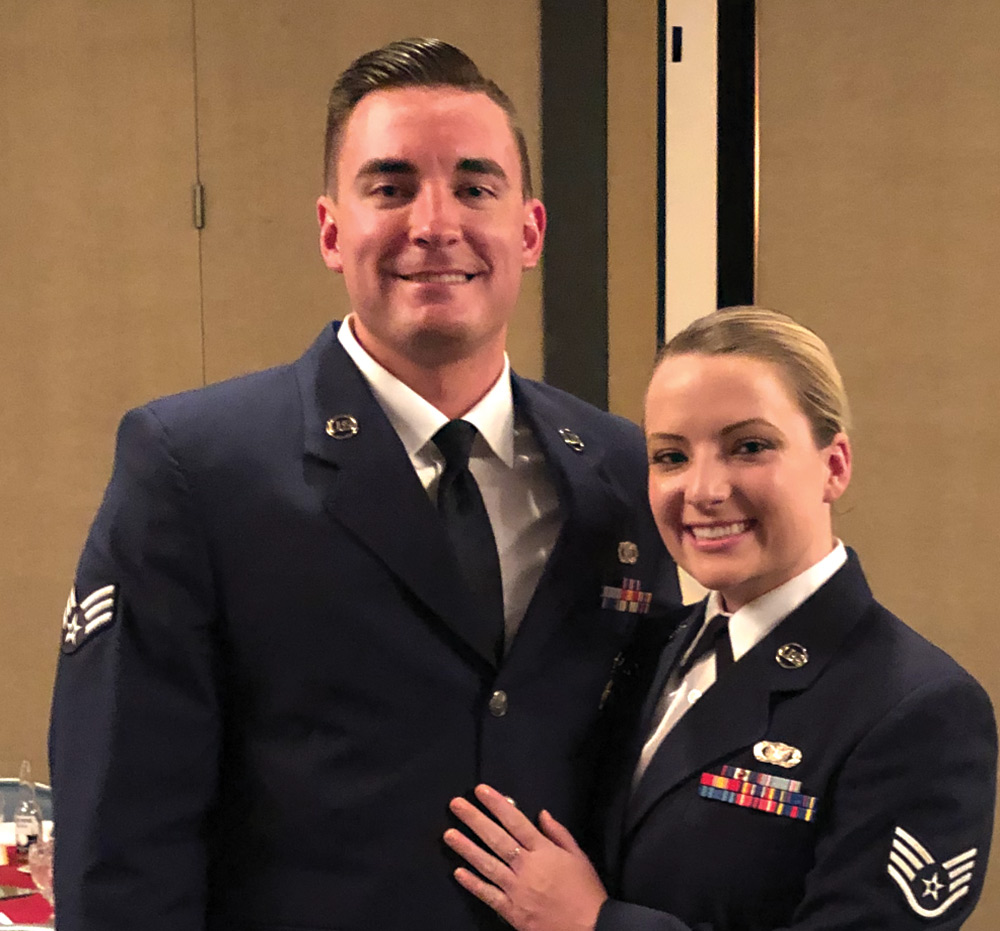 Portrait close-up indoor photograph view of Aaron & Peyton Heintzelman in their navy blue United States Air Force military vests smiling as they are standing next to each other in what appears to be a conference ballroom area of some sort