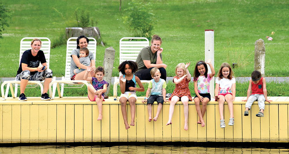 group of kids sitting on a boating dock with their parents behind them