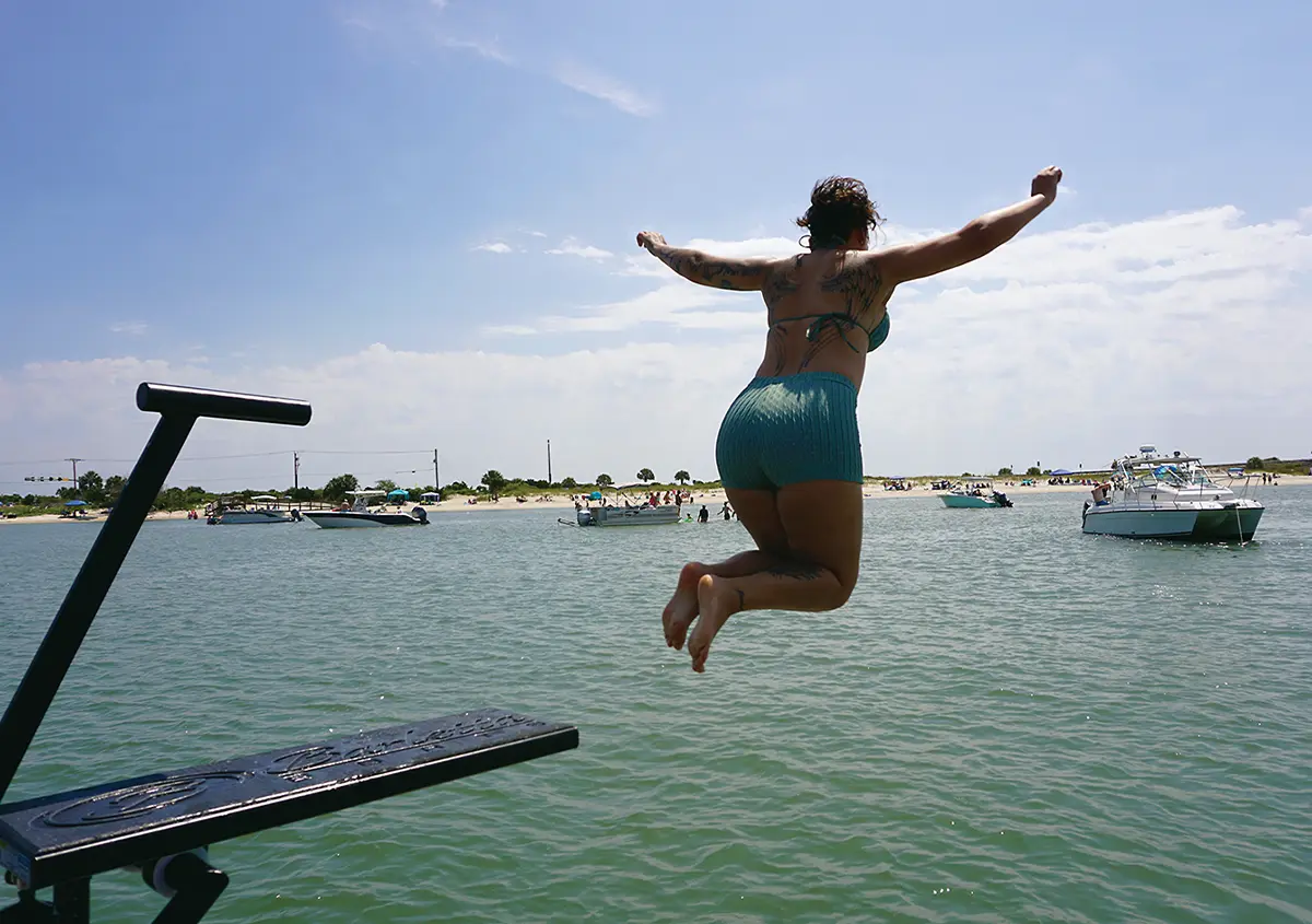 back view of a woman jumping into water from the dive board of a sailing pontoon