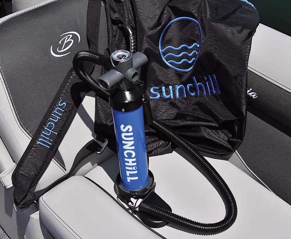 Portrait close-up photograph view of the Sunchill Water Hammock product accessories which contain the following: dark blue/black dual-action pump and a dark blue/black carrying bag as both of these items are sitting on top of a light faded grey pontoon motorboat vehicle leisure chair