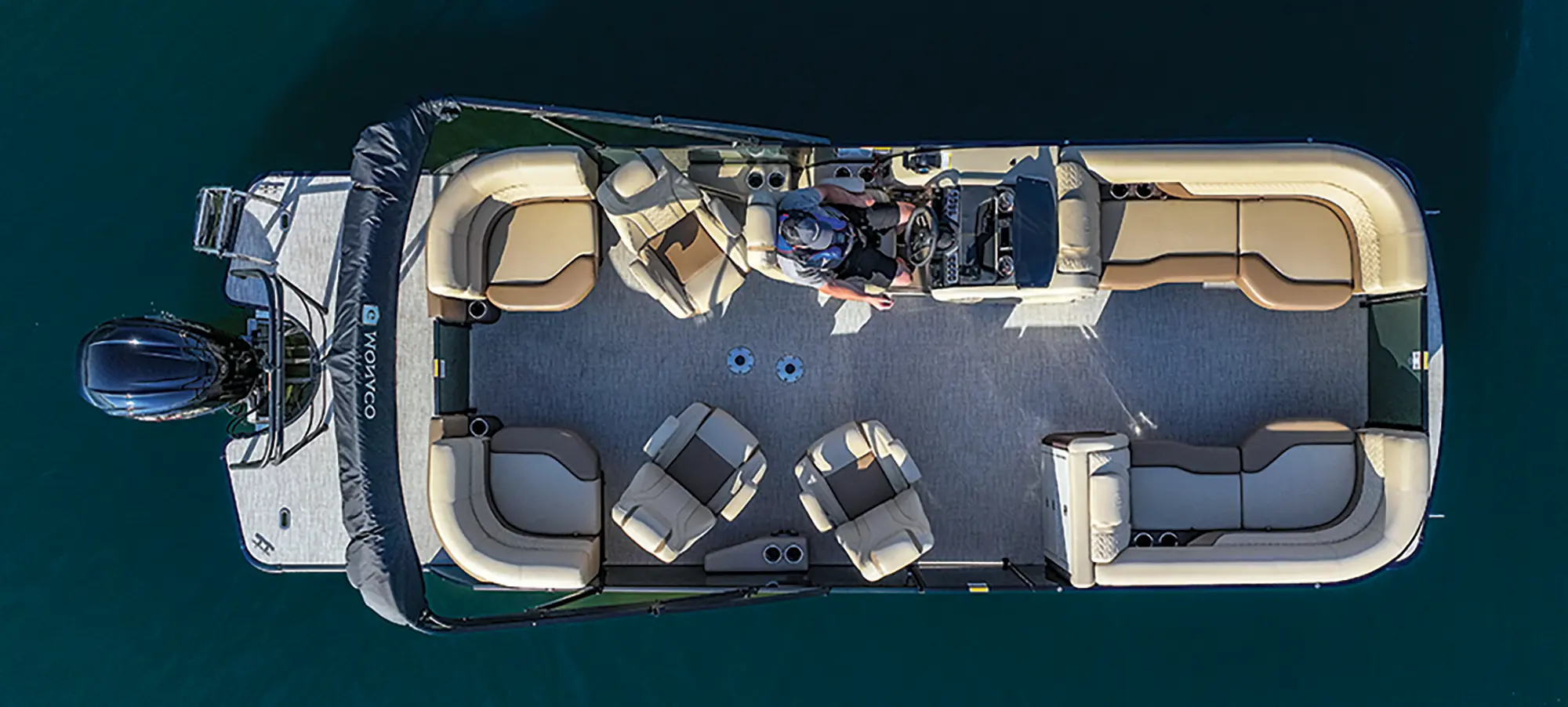 Top aerial drone-shot outdoor landscape photograph of the Godfrey Monaco 235 QS pontoon motorboat vehicle showcasing the male driver seated in the driver's seat as the vehicle is out in the water