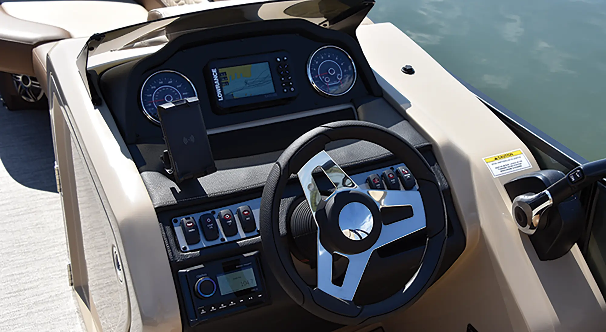 Angle landscape photograph of the Godfrey Monaco 235 QS pontoon motorboat vehicle featuring the driver's wheel, driving dashboard controls, gauge meters, radio controls, and other various random key assorted controls