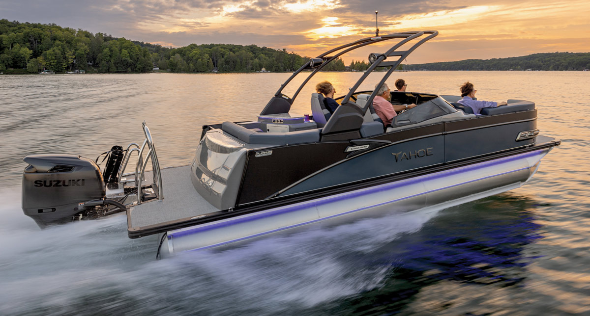 A modern motorboat with passengers cruising on a lake at sunset.