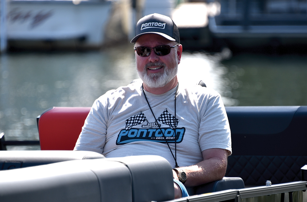 A man smiling on a boat, wearing sunglasses and a cap.