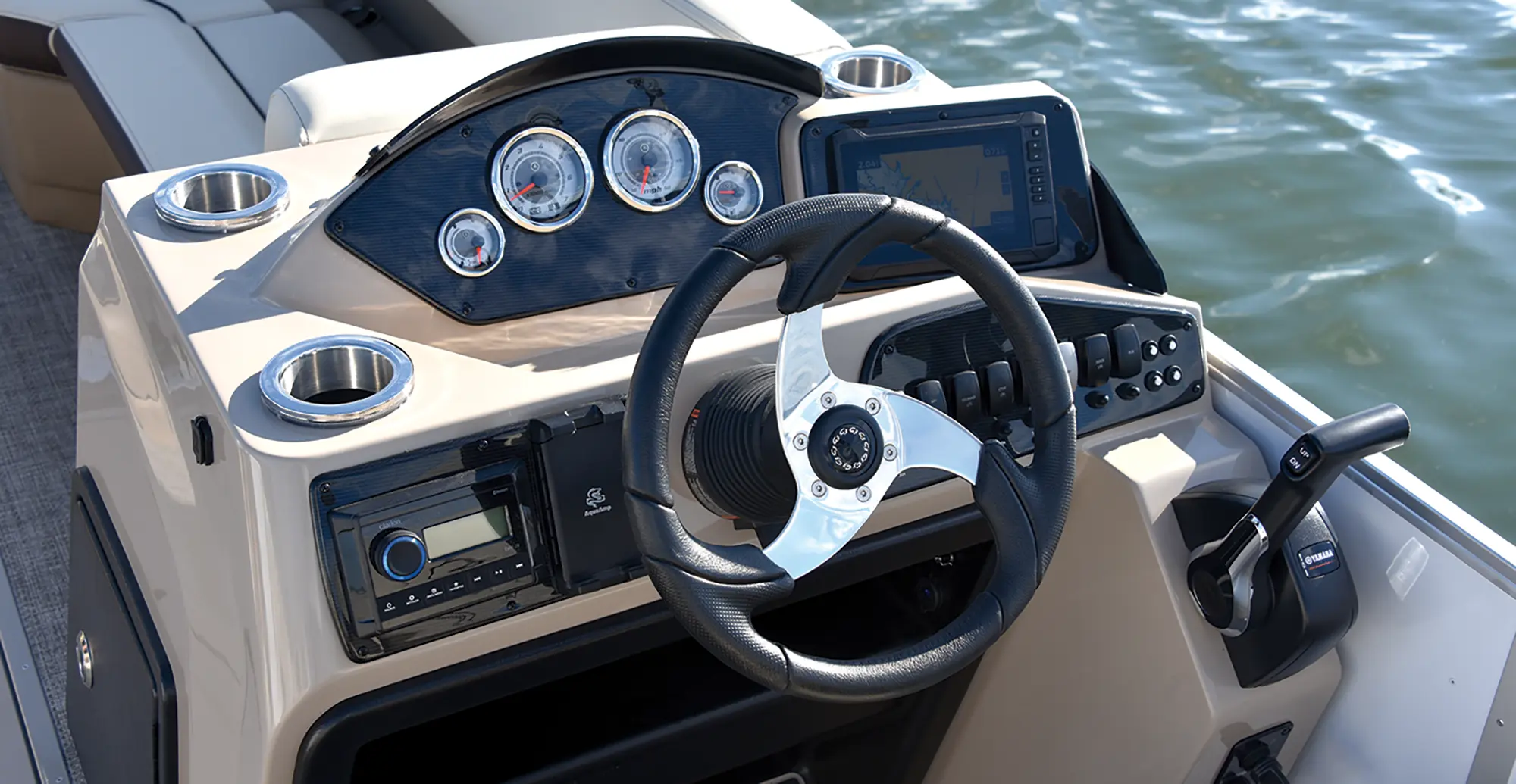 Angle landscape photograph of the SunCatcher Select 324 SL pontoon motorboat vehicle featuring the driver's wheel, driving dashboard controls, gauge meters, radio controls, and other various random key assorted controls