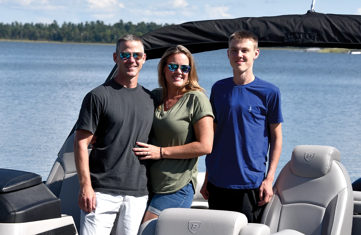 a man, a woman and a young man stand together for a group photo on a pontoon on water
