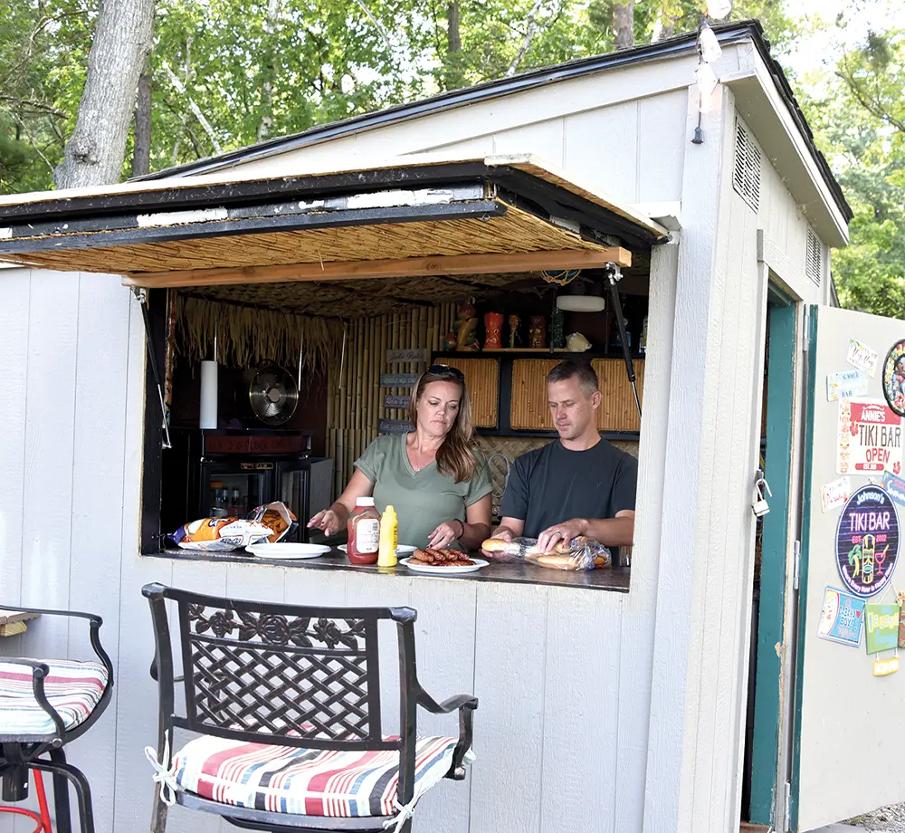 a man and a woman prepare link hotdogs in a shack like structure