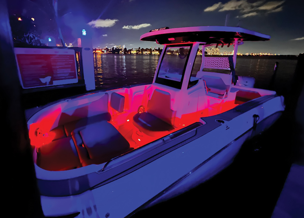 A modern boat with red interior lights docked at night, with city lights in the background.