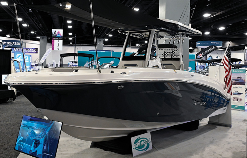 A dark blue and white motorboat with a "NEW MODEL" sign displayed indoors at a boat show.