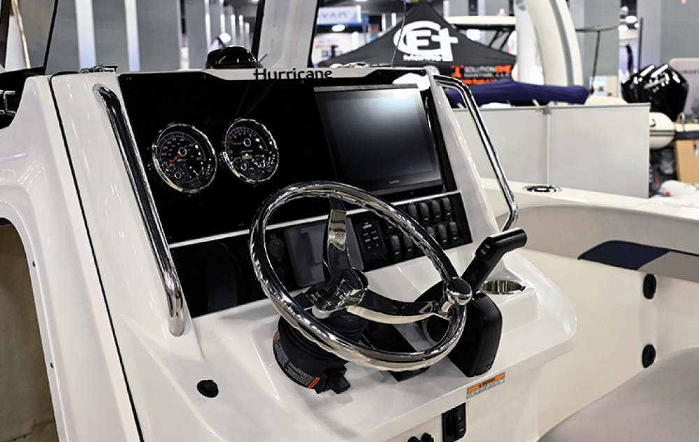 Close-up of a boat's control console with gauges, a screen, and a steering wheel.