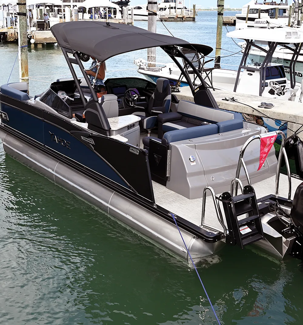 A pontoon boat docked at a marina with a black canopy and seating.