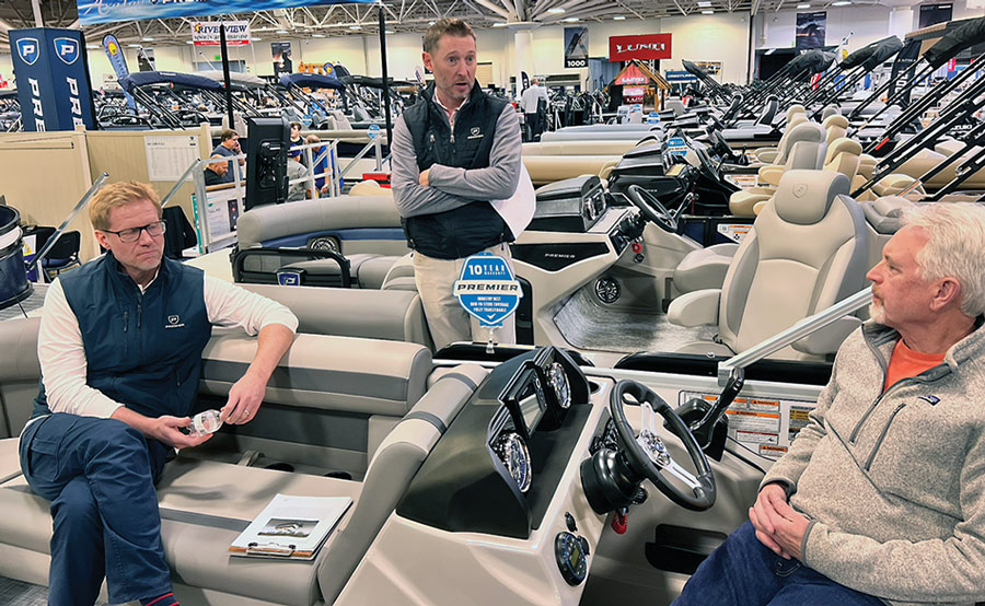 three men stand among the Premier Sunscape pontoon's on display while deep in conversation